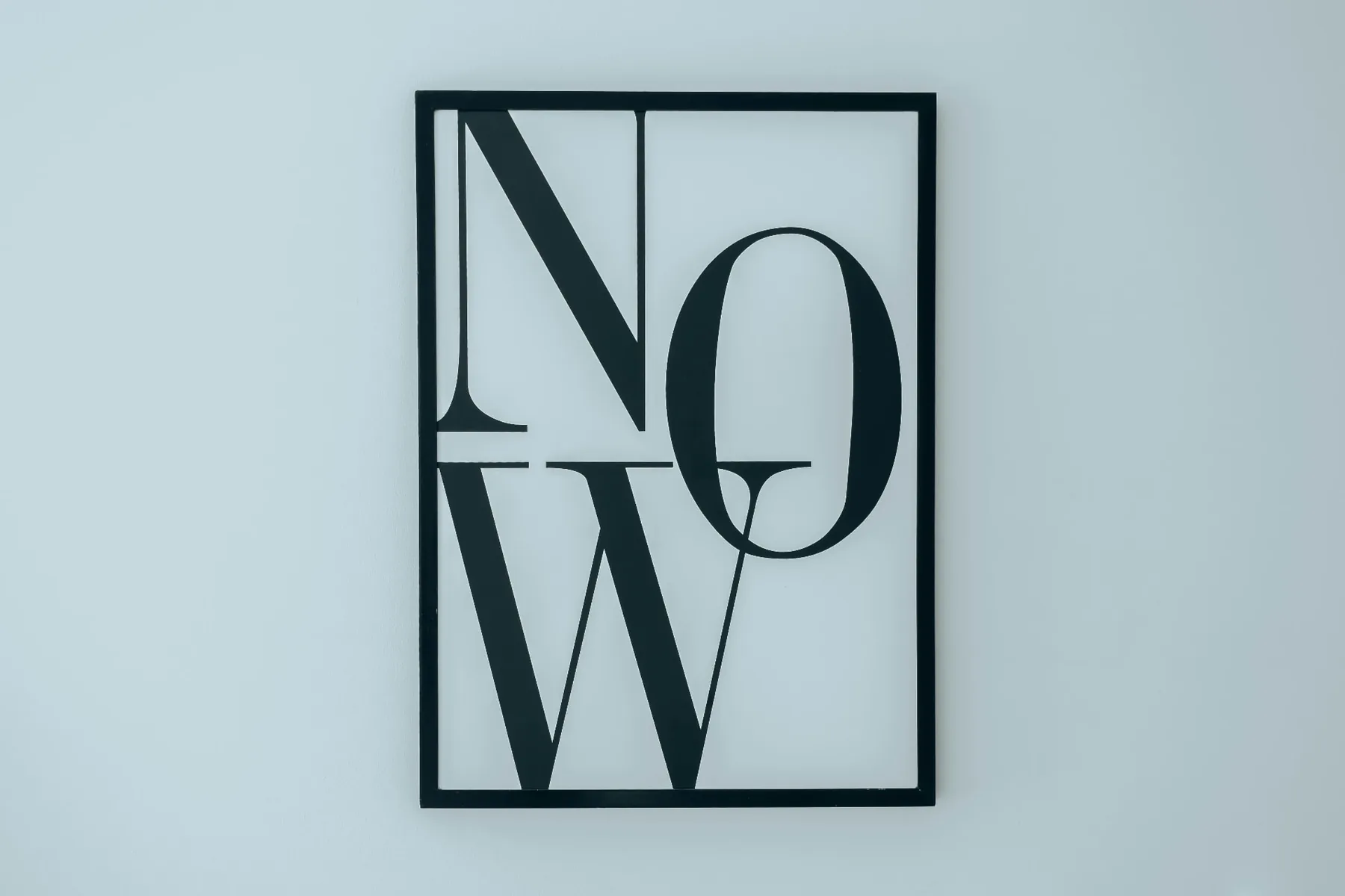 Typografie-Kunstwerk NOW in schwarzem Rahmen auf hellem Hintergrund